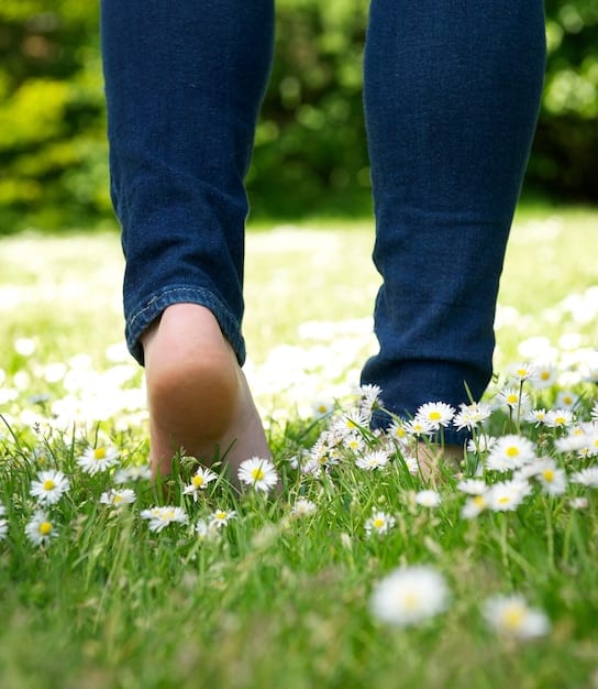 A close-up of bare feet walking on a grassy path, illustrating the simple act of connecting with the earth and grounding oneself.