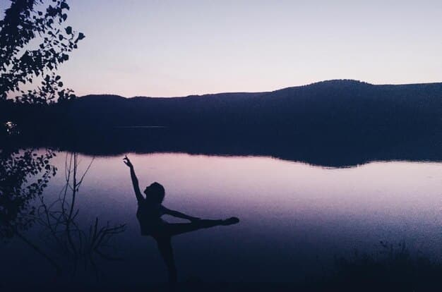 A person practicing yoga at sunrise overlooking a tranquil lake, highlighting the connection between physical activity and inner peace.