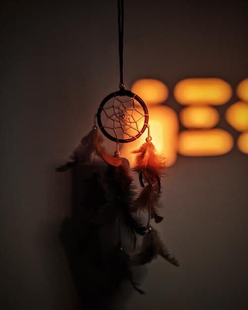 A person journaling their dream in a dimly lit room with a dreamcatcher hanging nearby. The scene evokes a sense of introspection and mystery, highlighting the personal reflection aspect of dream interpretation.