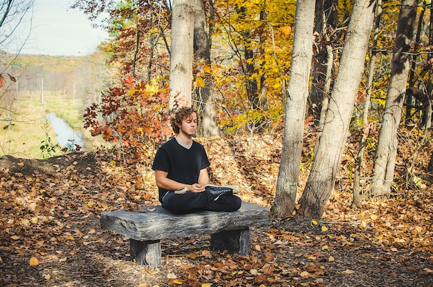 A serene scene of a person sitting in nature without any technology, meditating with eyes closed and a gentle smile. The background should feature lush greenery, sunlight filtering through trees, and a sense of complete peace and tranquility.