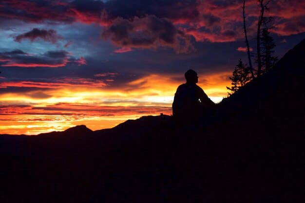 A silhouette of a person sitting cross-legged on a hill overlooking a sunset. The colors of the sky are warm and inviting, symbolizing hope and peace. The overall image conveys a sense of quiet contemplation and acceptance.