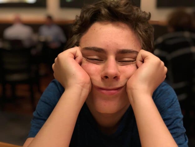 A close-up shot of a stressed student's face during a test, showing visible signs of anxiety like sweating, furrowed brow, and a trembling hand holding a pen. The test paper is blurred in the background to emphasize the student's distress.