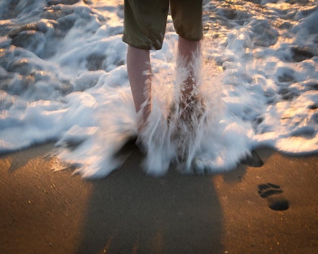 A person walking barefoot on a sandy beach, with waves gently lapping at their feet. The focus is on the sensory experience of connecting with the earth.