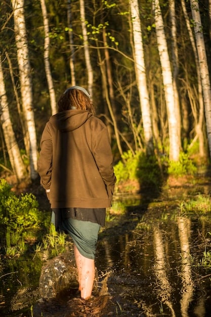 A person enjoying a peaceful nature walk in a forest with tall trees and dappled sunlight. The individual is smiling and appears relaxed, emphasizing the importance of connecting with nature for self-care.