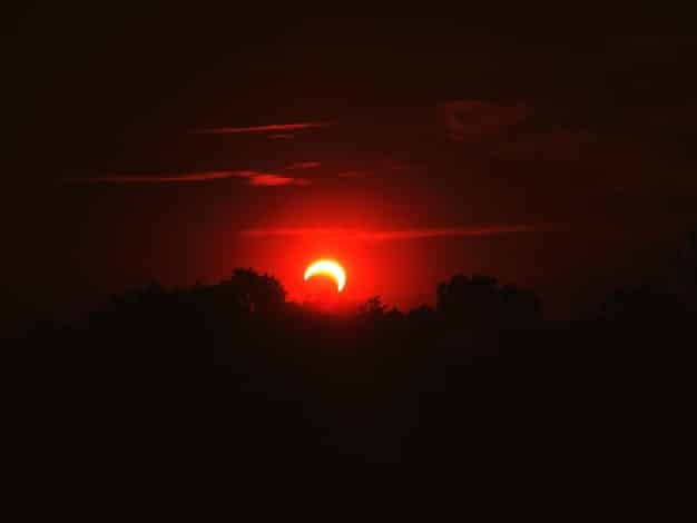 A dramatic photograph of a total solar eclipse, with the Sun's corona visible around the dark silhouette of the Moon.