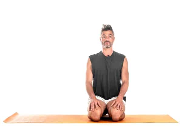 A person sitting cross-legged on a yoga mat, with their eyes closed and a peaceful expression on their face. The background is a softly lit room with plants and candles, creating a tranquil and inviting atmosphere. The focus is on the person's serene demeanor and inner calm.