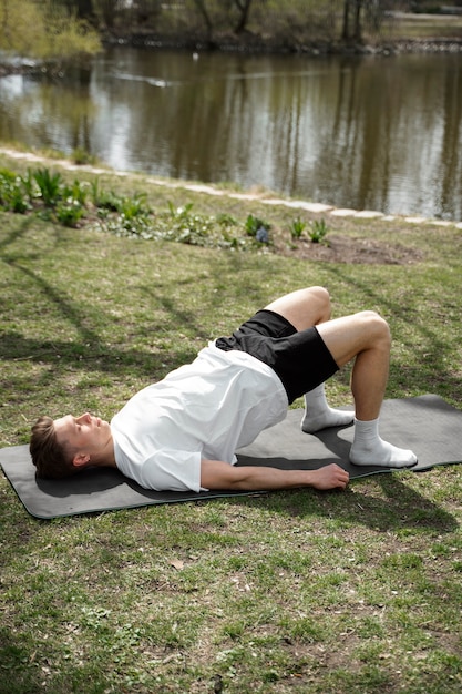A person lying on their back on a mat, performing progressive muscle relaxation, with focus on tensing and releasing leg muscles. A calm and serene environment is depicted.