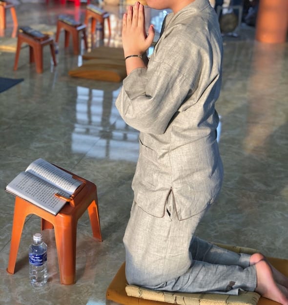 A person in the Burmese position, using a chair. Feet flat on the floor, maintaining proper posture. Demonstrate the Zafu cushion under the hips for additional support.
