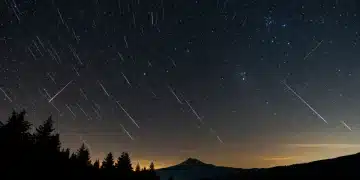 Vibrant meteor shower in a dark night sky over mountains