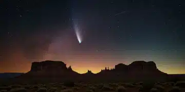Bright comet with a long tail against a starry night sky over a mountainous landscape.
