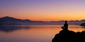 Sunrise over mountains with a person meditating, symbolizing spiritual awakening and inner peace.