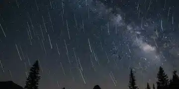 Vibrant Perseid meteor shower streaking across a dark night sky above a silhouetted landscape.